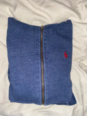 Blå hoodie från Polo Ralph Lauren XS - Blå hoodie från Polo Ralph Lauren i storlek XS. Tröjan har huva med vit snörning, hel dragkedja framtill och rött broderat Polo-logo på bröstet. Mjuk insida och klassisk känguruficka. Perfekt för chill dagar och streetstyle. Lite liten i storleken men är varm och skön till vintern. Knappt använd alls då jag vuxit ur den för länge sen!