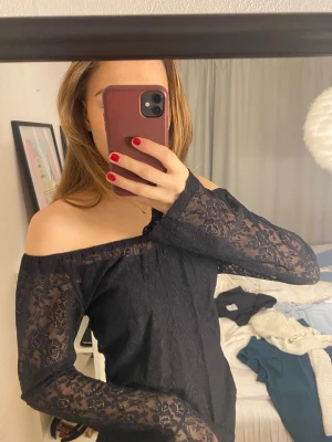 Svart spetsblus - Säljer en svart offshoulder blus med långa ärmar i genombruten spets. Blusen har en rak passform och är helt täckt av ett blommigt spetsmönster. Perfekt för dig som gillar en stilren men ändå romantisk look.