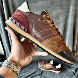 Valentino Rockrunner sneakers brun - Snygga Valentino Rockrunner sneakers i olika nyanser av brunt, vinrött och beige. Skorna har detaljer i mocka och skinn, samt ikoniska pyramidnitar vid hälen. Rund tå, snörning och platt sula ger en cool och sportig vibe.