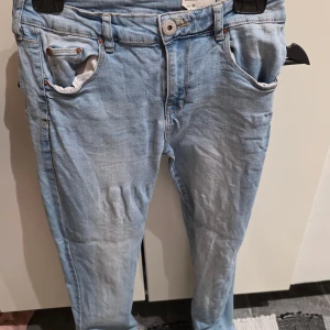 Ljusblå skinny jeans storlek M - Säljer ett par ljusblå skinny jeans från 157 i storlek M. Jeansen har klassisk femficksdesign, bälteshällor och knappstängning framtill. Materialet är mjukt denim med snygga slitningar och kontrastsömmar. Perfekt för dig som gillar smal passform och ljus tvätt.