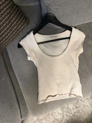 Vit croppad T-shirt  från zara - Säljer en vit croppad T-shirt  från zara med rund halsringning och ärmlös design. Toppen är gjord i mjuk bomull och har en clean, enkel look som är lätt att matcha med allt. Perfekt för dig som gillar minimalistisk stil.