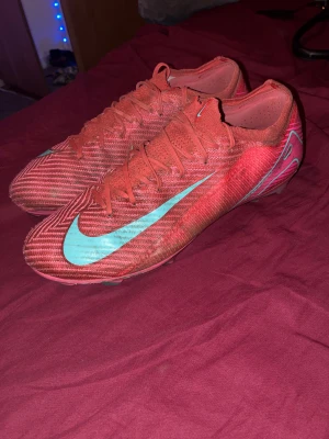 Nike Mercurial fotbollsskor rosa/turkos - Säljer ett par Nike Mercurial fotbollsskor i en riktigt snygg rosa färg med turkosa detaljer och logga. Skorna har snörning, platt sula med dobbar och är tillverkade i syntetmaterial. Perfekta för dig som vill sticka ut på planen!