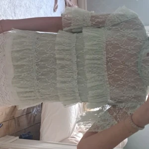 Vit spetströjs med volanger - Säljer en superfin vit kortklänning med spets och volanger. Klänningen har genomgående spetsmönster, höga volanger och är kortärmad med transparenta detaljer. Perfekt för dig som gillar romantisk och feminin stil.