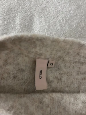 Beige oneshoulder stickad topp från Nelly - Säljer en beige stickad topp från Nelly i storlek XS. Modellen är oneshoulder med korta ärmar och har en mjuk, lite fluffig stickad struktur. Ser ut som den mörkblå tröjan fast i begie.
