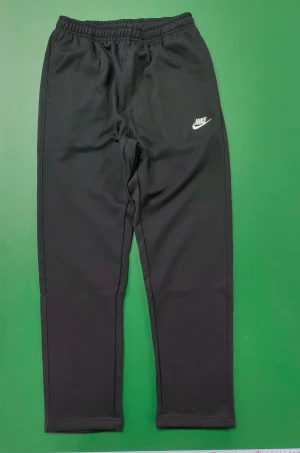 Svarta mjukisbyxor från Nike, M - Svarta mjukisbyxor från Nike med vit logga på vänster lår. Byxorna har elastisk midja och en bakficka. Tillverkade i polyester med bomullskant vid fickan. Perfekta för chill eller träning.