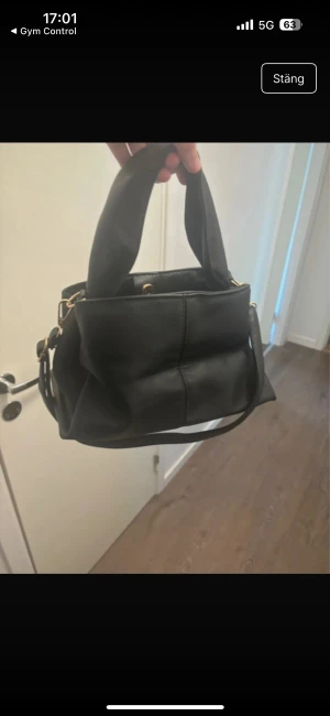 Svart handväska  med axelrem - Söt handväska som endast är använd en gång, se bild 3, har ett hål på insidan som ej syns utifrån. Säljs billigt vid snabb affär