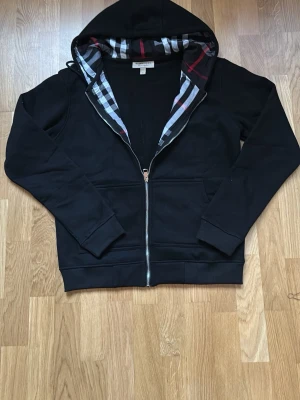 Svart burberry hoodie - Elegant svart Burberry-hoodie med tidlös design. Mjuk och bekväm med stilren look som funkar perfekt till både vardag och mer uppklädda outfits.  ⭐ Skick: Mycket bra  📏 Storlek: M 🎨 Färg: Svart 👕 Passform: Normal 📦 Snabb och säker frakt  Hör av dig vid frågor eller om du vill ha fler bilder. 
