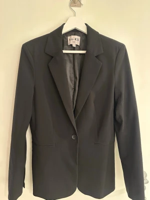 Kavaj NA-KD - Stilren svart kavaj från NA-KD med klassisk krage och en knapp framtill. Jackan har två fickor och är helfodrad.