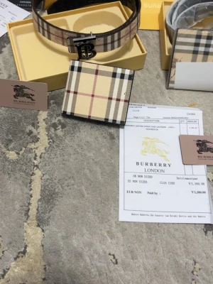 Rutig plånbok med bälte set från Burberry - Säljer en snygg plånbok från Burberry med klassiskt rutig design i beige, svart, vit och röd. Plånboken är tillverkad i skinn och har en stilren look som passar perfekt för dig som gillar lyxiga accessoarer med ikonisk känsla.