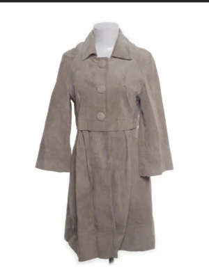 Beige mocka trenchcoat/kappa från Hallhuber - Snygg beige trenchcoat/kappa från Hallhuber i äkta mocka med bred krage och stora knappar framtill. Jackan har långärmade ärmar och markerad midja för en schysst siluett. Perfekt för dig som vill ha en stilren och tidlös look. Snygg och skön att bära! 