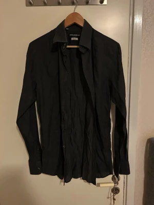 Svart skjorta från Dolce & Gabbana - Svart skjorta från Dolce & Gabbana Gold, med klassisk krage och långa ärmar. Skjortan har knappar framtill och är tillverkad i ett mjukt bomullstyg som känns skönt mot huden. Perfekt för dig som gillar stilrena och exklusiva plagg.