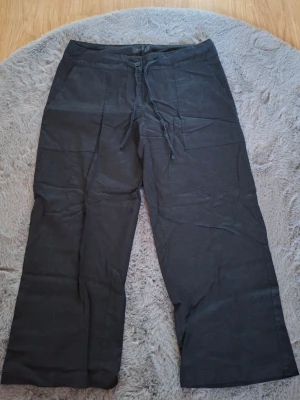 Svarta korta linnebyxor från Estelle, strl 40 - Svarta korta linnebyxor från Estelle i storlek 40. Byxorna har raka ben, snörning i midjan och praktiska fickor både fram och bak. Materialet är linne vilket gör dem luftiga och sköna. Perfekt för dig som gillar en chill och enkel stil.