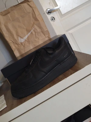 Nike Air Force 1 svart sneaker - Säljer ett par svarta Nike Air Force 1 sneakers med klassisk låg siluett. Skorna har snörning, rund tå och är tillverkade i skinn med meshdetaljer på sidan. Snyggt ton-i-ton med svart sula och diskret Nike-logga. Perfekt för dig som gillar stilrena och tidlösa sneakers. Och dem är köpta i en butik i Stockholm för ungefär 4 månader sedan 