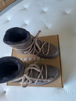 Nya taupe Inuikii boots med snörning - Överdel: 60% lammskinn 40% koskinn foder: 100% lammskinn innersula: 100% polyuretan innersula foder: 100% lammskinn yttersula: 100% eco gummi Varmfodrade Produktinformation Snördetaljerna ger dessa vinterstövlar en distinkt touch. Designade för värme och stil, de har en robust sula och ett mjukt innerfoder för extra komfort. Viktiga funktioner Ger värme i kallt väder Erbjuder en säker och justerbar passform med snörning Hållbar sula för bra grepp 