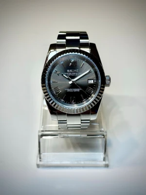 Seiko mod 39mm - Datejust - Helt oanvänd Seiko Datejust mod med grå urtavla med romerska siffror. Utrustad med Seikos NH35 urverk, med hållbart safirglas och en gridlock clasp. som gör det lätt att justera klockans längd. DM mig om du vill ha fler bilder eller undrar något. Extra länkar följer också med. Pris är diskuterbart.