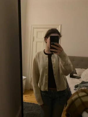 Beige kofta från & Other Stories - Supermjuk och mysig beige kofta från & Other Stories, med rund halsringning och stora knappar framtill. Koftan är stickad och har lång ärm samt en lite croppad passform. Perfekt att slänga över en t-shirt eller linne. Något nopprig men det går att fixa!