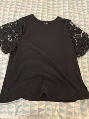 Svart blus med spetsärmar - Säljer en svart blus från vero Moda med korta ärmar i vacker spets. Toppen har rund hals och en loose passform. Ärmarna är dekorerade med blommig spets som ger en extra detalj till looken. Perfekt för dig som gillar stilrena plagg med twist.