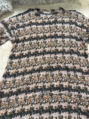 Mönstrad klänning från Masai XL - Säljer en cool klänning från Masai i storlek XL med ett unikt geometriskt mönster i beige, svart och bruna toner. Klänningen har korta ärmar och är gjord i ett mjukt och lätt material som känns skönt mot huden. Perfekt för dig som gillar att sticka ut med mönster.