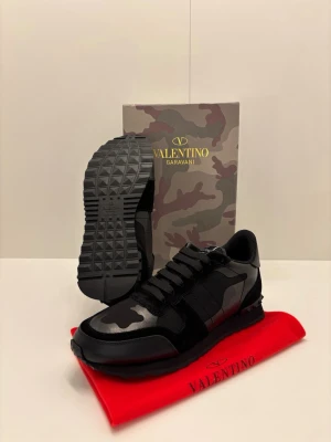 Valentino Rockrunner Storlek 43 - Säljer ett par exklusiva Valentino Rockrunner i storlek 43, i mycket fint skick. Svart camo, premiumläder och mocka. Levereras med originalkartong och tillbehör. Stilrena, bekväma och ikoniska sneakers för dig som vill lyfta din outfit.