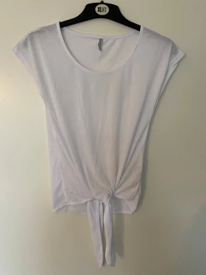 Vit knyt-topp från Fishbone XS - Säljer en vit topp från Fishbone i storlek XS. Modellen har korta ärmar, rund halsringning och en snygg knytning framtill som ger en chill vibe. Tunn och mjuk bomull, perfekt för varma dagar eller lager-på-lager. Enkel och stilren design. Endast provad och tvättad. 