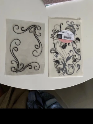 Scrapbooking pyssel material dekorationer - Säljer scrapbooking dekorationer /pyssel 1 st svart (pärlor med klister på baksidan) ringtones i ett färdigt  mönster och rub ons i  blommiga inslag och tunna linjer. (Man sätter fast på önskat papper genom att gnugga fast dekorationen.  Nyskick och aldrig använt.