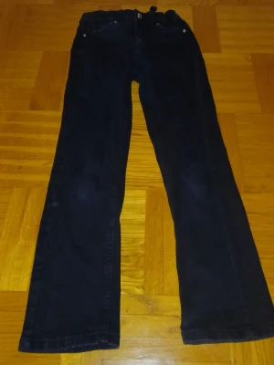 Mörkblå bootcut jeans med justerbar midja - Säljer ett par mörkblå jeans med bootcut passform och klassiska fem fickor. Byxorna har justerbar resår i midjan för extra komfort och silverfärgade nitar. Materialet är jeans och färgen är riktigt mörkblå, perfekt till sneakers eller boots.