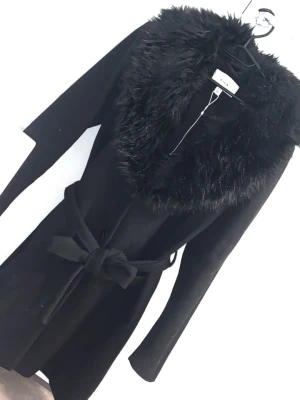 Svart kappa med fuskpäls från Vila - Snygg svart kappa från Vila med stor krage i fuskpäls och knytbälte i midjan. Långärmad och med klassisk siluett, perfekt för dig som vill ha en elegant look. Pälsdetaljen ger extra lyxig känsla och kappan har en stilren design.