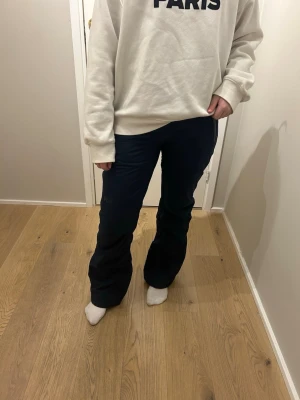 Blåa täckbyxor från Helly Hansen - Säljer ett par blåa täckbyxor från Helly Hansen med bootcut-snitt. Byxorna har dragkedjor vid fickorna och knappar i midjan. Materialet är slitstark syntet som tål kyla och väta, perfekt för vinteraktiviteter. Snygg och enkel design med HH-logga på benet. Dom har lufthål på insidan av låren.  Köpta förra säsongen och andvända en gång