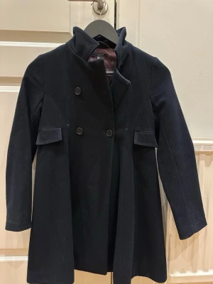 Svart kappa från Little Marc, stl 10A - Snygg marinblå kappa med dubbelknäppning och hög krage från Little Marc (Marc Jacobs). Jackan har långa ärmar, fickdetaljer och ett brunt foder med blommigt mönster. Plisserad rygg ger extra schysst siluett.