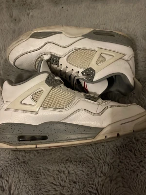 Nike Air Jordan 4 Retro Oreo - Nike Air Jordan 4 Retro Oreo sneakers i vit och grå färg med röda detaljer under sulan. Skorna har meshpaneler på sidorna, synlig luftdämpning och speckled grå midsole. Tillverkade i skinn och syntetmaterial med snörning och platt sula.   (Har ingen orginalbox)
