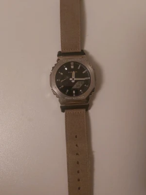 G-shock casio  - En G-shock i fint skick, väldigt hållbar och vattentät, perfekt för alla fysiska aktiviteter och sporter. Har många extra funktioner så som larm och timer. Visar datum. olivgrönt/"camo" färgat band, silver/stål färgad kant och svart urtavla. Nypris cirka 3000kr