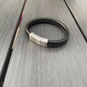 Svart läderarmband med metallspänne - Snyggt svart armband i flätat läder med ett stilrent, matt metallspänne. Perfekt accessoar för dig som gillar minimalistisk och modern stil. Spännet har en diskret gravyr och armbandet är bekvämt att bära hela dagen. Aldrig använt