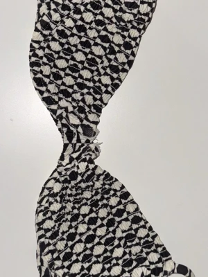 Svartvit rutig bikiniöverdel - Säljer en bikiniöverdel med svartvitt rutigt mönster och justerbara axelband. Materialet är mjukt och stretchigt, med vadderade kupor och smockad yta. Perfekt för dig som gillar grafiska mönster och vill sticka ut på stranden. Storlek 70B