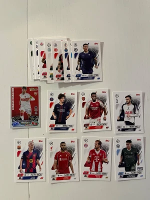Samling fotbollskort Topps Champions League - Säljer en bunt fotbollskort från Topps Champions League-serien. Blandade spelare från kända klubbar som Bayern München, PSG, Arsenal, Tottenham, Barcelona, Liverpool och fler. Flera kort har snygga färger och detaljer, vissa med glittrig finish och specialdesign. Har bara öppnat men vill inte ha just dem här korten. Harry Kane är med En av världens bästa fotbollsspelare. 