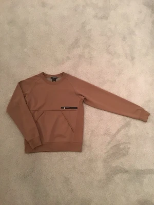 Beige sweatshirt från Sail racing  - Snygg beige sweatshirt från Sail racing med rund hals och lång ärm. Tröjan har en cool detalj med svart patch och ficka framtill. Materialet känns mjukt och har en clean look som passar bra till olika stilar. Perfekt för dig som gillar stilrena plagg. Tröjan ändats använd ett fåtal gånger.