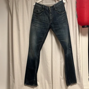 Mörkblåa jeans från Denham  - Säljer ett par blå jeans från Denham med snyggt slitna detaljer och raka ben. Jeansen har klassisk femficksdesign, knappgylf och coola kontrastsömmar. Materialet är robust denim i bomull och passformen är rak. Perfekta för dig som har en avslappnad stil. Cond: 9/10 och storlek 31/34. Priset är ej suttet i sten!!!