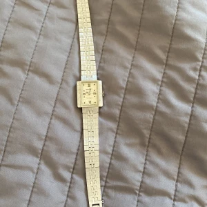 Orient rektangulär guldfärgad klocka - Snygg vintage klocka från Orient med rektangulärt ur och guldfärgat armband i metall. Urtavlan har romerska siffror och en diskret textur. Länken har ett unikt geometriskt mönster som ger klockan en cool retrovibe. Perfekt för dig som gillar klassisk stil med en twist.