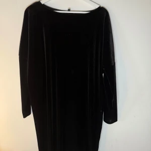 Svart långärmad klänning Ilse Jacobsen - Snygg svart klänning från Ilse Jacobsen med lång ärm och rak, loose passform. Materialet är mjuk och glansig polyester med elastan som ger en skön stretch. Perfekt för dig som gillar minimalistisk stil och vill ha en enkel men elegant look. Storlek S/M men mer en M