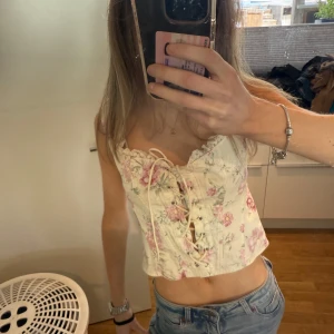 Blommig korsett-topp med snörning - Supersöt korsett-topp i ljusbeige med blommigt mönster i rosa och grönt. 