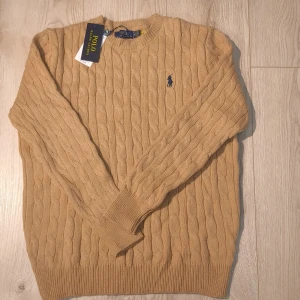 Sandfärgad Ralph Lauren Knit M - Stickad Ralph Lauren tröja i sandfärg med den klassiska Polo-loggan på bröstet. Tillverkad i 100% mjuk bomull som sitter bekvämt och håller formen fint. 📏Storlek M, längd 65 cm och bredd 48,5 cm. Oanvänd i fint skick. Meddela för frågor!