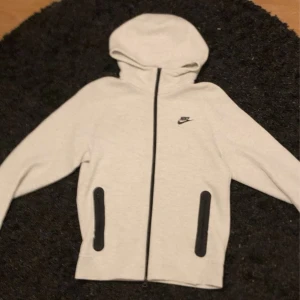 Nike ljusgrå mjukisbyxor med snörning - Nike mjukisbyxor i ljusgrått med svarta detaljer och snörning i midjan. Byxorna har raka ben, elastisk midja och svarta dragkedjor på fickorna. Perfekta för chill eller träning, med klassisk Nike-logga på låret.