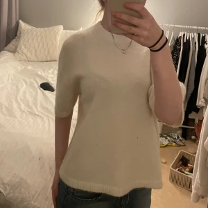 Vit stickad tröja från WEEKDAY - Supermjuk vit stickad tröja från WEEKDAY med kort ärm och rund hals. Tröjan har en enkel och clean look med ribbade kanter vid hals, ärmslut och nederkant. Perfekt för lager-på-lager eller som den är till jeans.