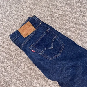 Levi's 501 mörkblå jeans straight fit - Klassiska Levi's 501 jeans i mörkblå denim med raka ben och femficksmodell. Snygga kontrastsömmar och ikonisk läderpatch bak. Jeansen är tillverkade i bomull och har en liten slitning på bakfickan. Perfekta för dig som gillar tidlös stil.