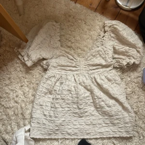 Vit puffärm blus med struktur - Supersöt vit blus med puffiga korta ärmar och v-ringning. Tyget är strukturerat och ger en cool, trendig look. Perfekt för dig som gillar romantiska vibes och volym. Passar till både jeans och kjol.