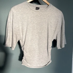 Ljusgrå croppad t-shirt Gina Tricot - Ljusgrå croppad t-shirt från Gina Tricot med korta ärmar och snygg snörning i sidan. Ny skick men använd några gånger. Ordinarie pris 250. Pris går att diskuteras.💞