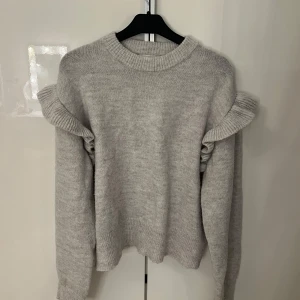Ljusgrå stickad tröja med volang - Säljer en jätte söt stickad tröja från Gina Young med volanger på armarna. Endast använd ett par få gånger så i mycket bra skick.