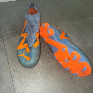 Fotbollsskor puma  - Säljer ett par grymma fotbollsskor från Puma i blått och orange. Skorna har en stickad, strumpliknande ovandel och coola detaljer i orange, inklusive Puma-loggan. Sulan har fasta dobbar för bra grepp på planen. Perfekta för dig som vill sticka ut på matchen!