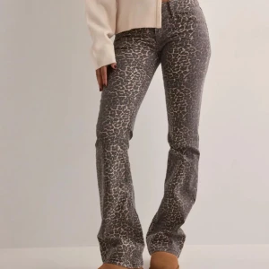 Leopardmönstrade bootcut jeans - Snygga jeans med leopardmönster i grå och beige toner. Modellen har bootcut-ben och klassisk femficksdesign med dubbla silverknappar i midjan. Perfekta för dig som vill sticka ut med en trendig look.