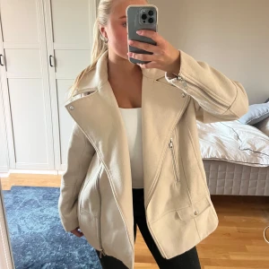 Beige kort kappa  - Snygg beige kappa med bred krage och coola silverfärgade dragkedjor. Jackan har lång ärm, fickor med lock och är tillverkad i ett mjukt ull-liknande material. Använt skick men fortfarande fin!