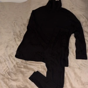 Svart ribbad polotröja - Svart ribbat set – polotröja & byxor 🖤  Ett stilrent och bekvämt set med långärmad polotröja och matchande byxor. Tillverkat i mjukt, stretchigt material som sitter skönt och följer kroppen. Den klassiska ribbade designen gör det lätt att styla – perfekt både till vardags och när du vill klä dig enkelt men snyggt ✨ 